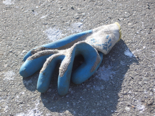white knitted work glove with blue rubberized palm on paint-spattered pavement
